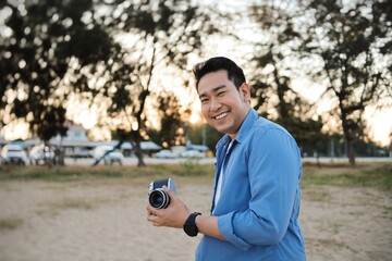 Asia man in blue shirt walking on the beach with vintage camera.