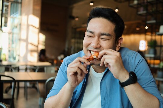 Happy  Asian Man Eating BBQ Chicken Wings In Restaurant.