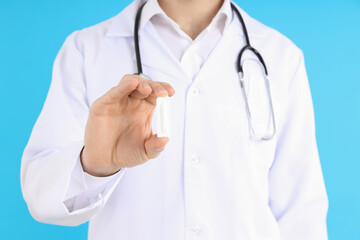 Doctor holds suppository on blue background. Hemorrhoids concept