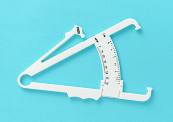 White caliper on blue background. Overhed. Slimming treatment concept.
