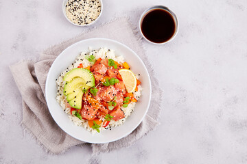 Poke bowl with salmon, rice, avocado, sesame seeds, micro greens, pepper and soy sauce on grey...