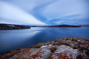 Colorful sunset on Lake Baikal at the beginning of winter. The Small Sea in December. Open calm water in the lake, view of the hills and mountain landscape, beautiful clouds in the sky.