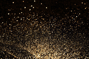 Black festive background. Abstract scattering of gold sparkles on black. Holiday backdrop, selective focus