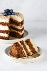Piece of vegan carrot cake with coconut cream, blueberries, walnuts and spices on a plate. Sugar, gluten and lactose free.