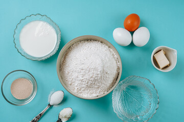 Baking ingredients for dough - white flour, eggs, milk, yeast, sugar, salt - on blue surface