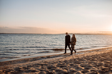 Young beautiful couple on a walk by the sea in autumn in the off-season, hugging, walking, smiling