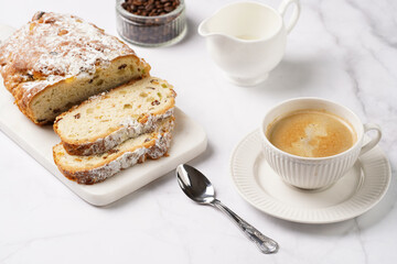 White porcelain cup with coffee cappuccino on a white saucer plate and christmas pastry stollen on a marble table