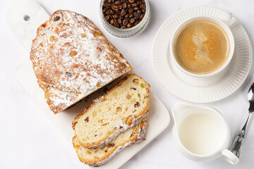 White porcelain cup with coffee cappuccino on a white saucer plate and christmas pastry stollen on a marble table