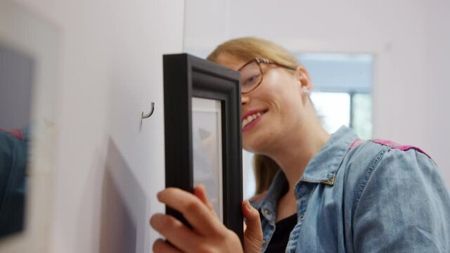Woman hanging a picture frame on the wall happily. close up view