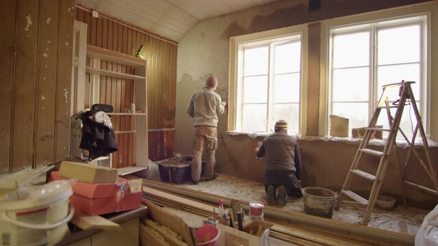 TRACKING ZOOM IN shot of 2 men plastering walls with clay, home improvement