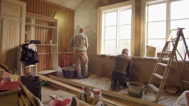 TRACKING shot R2L ZOOM OUT of 2 men plastering walls with clay, DIY
