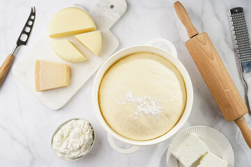 Various cheese types on marble and porcelain plates and fresh dough - ingredients for traditional georgian open pie khachapuri
