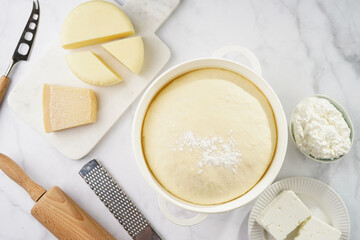 Various cheese types on marble and porcelain plates and fresh dough - ingredients for traditional georgian open pie khachapuri