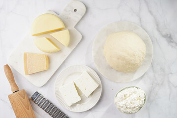 Various cheese types on marble and porcelain plates and fresh dough - ingredients for traditional georgian open pie khachapuri