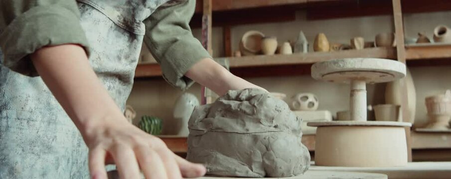 Young female sculptor using wire to cut off piece of clay during workday in pottery workshop