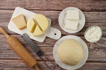 Various cheese types on marble and porcelain plates and fresh dough - ingredients for traditional georgian open pie khachapuri