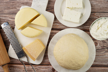 Various cheese types on marble and porcelain plates and fresh dough - ingredients for traditional...