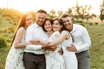 a family of different ages hugs tightly being in nature at sunset. family with five people happy together. portrait of a middle aged family. a group of people
