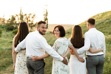 a family of different ages hugs tightly being in nature at sunset. family with five people happy together. portrait of a middle aged family. a group of people