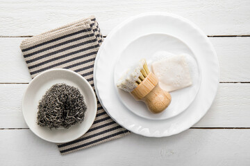 Solid dish washing soap, covered with foam. Zero waste lifestyle. Dishwashing soap on pile of plates with foamy kitchen cleaning sisal bamboo round dish brush. Minimalist white wood background. 