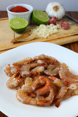 Raw shrimp. Raw fresh prawns with ingredients like lemon, garlic, paprika and bay leaves in the background.