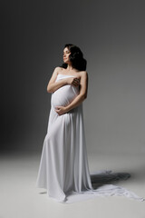 Fototapeta na wymiar Caucasian young beautiful pregnant woman with dark hair in white fluttering fabric posing on a white background. isolates the banner space for text. Antique style