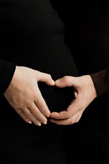 A man's and a woman's hand are folded on a pregnant woman's stomach