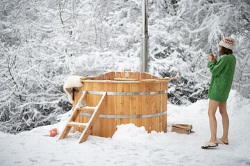 Woman taking photo of a wooden bath, during winter vacations at snowy mountains. Scandinavian...