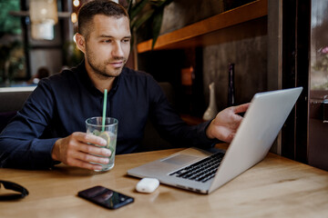 Young businessman is having online meeting on laptop in restaurant. Remote work.