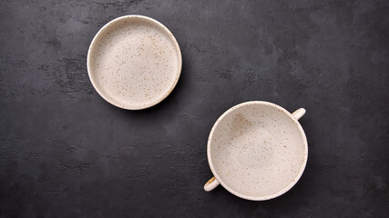 Flat lay deep soup bowl with handles and saucepan on black textured graphite background. Copy space