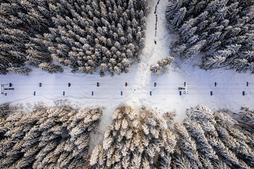 Alpine ski lift aerial drone view. Chairlift at ski resort, mountain winter forest top down rising shot. Pine trees covered with snow. Skiers and snowboarders carried up the hill. Active lifestyle.