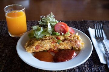 A Piece of Omelet served with fresh salad vegetables and sauces on a white plate with fresh orange juice on wooden table