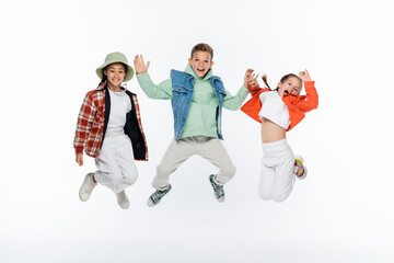 full length of stylish kids smiling while jumping on white.