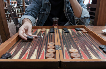 Close up man hand holding backgammon checker and playing backgammon at outside. Dices. Focus is on the hand. Front of the photo is blur.