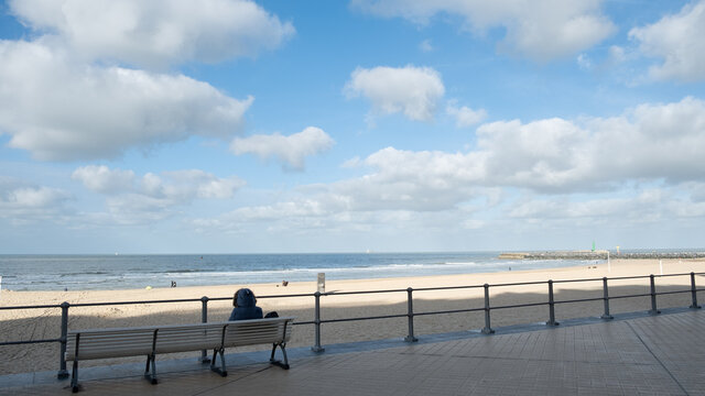 Woman with a grey coat on a bench in front of the beach and the norther sea, 
