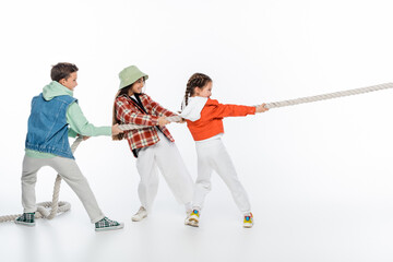 side view of happy preteen children pulling rope while playing tug of war game on white.