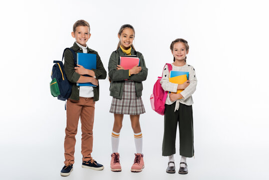 cheerful schoolboy and schoolgirls standing with backpacks and notebooks on white.