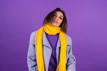 Young woman in a gray coat and a yellow scarf on a purple background posing, cozy and warm, autumn...