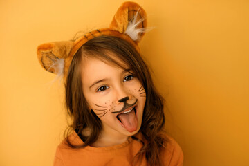 A child dressed up as a tiger with a painted mustache and a hat with ears growls and shows his...