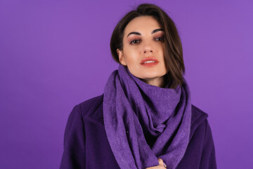 Young woman in a woolen coat and scarf on a purple background posing, cozy and warm, autumn-winter...