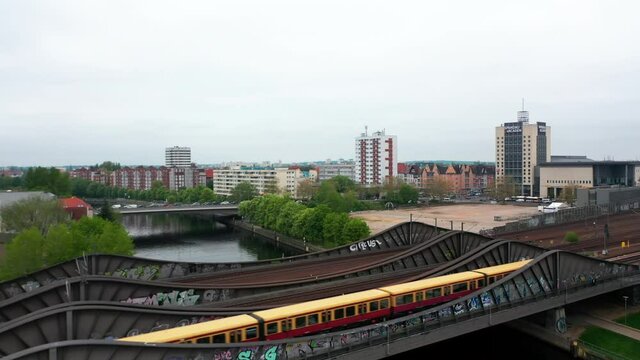 Fly over steel bridge over river in city. Suburban train running on multitrack railway line. Residential neighbourhood in background. Berlin, Germany