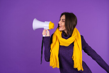 Young woman in a knitted dress and in a yellow scarf on a purple background cheerfully shouts into...