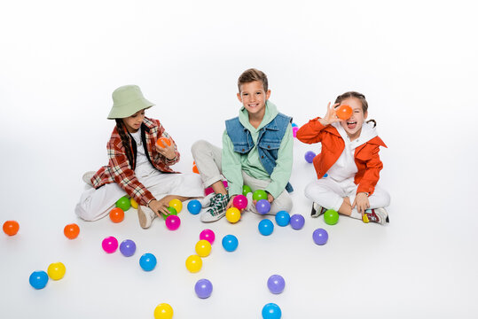 cheerful preteen kids sitting and playing with colorful balls on white.