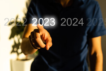 Finger pressing blue start 2023 button on virtual interface on gray background with copy space for text. Concept of new year. Businessman pressing 2023 start up business. Beginning of New Year 2023