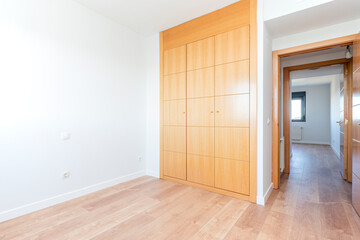 Empty bedroom with three section wardrobe in cherry wood with oak parquet flooring