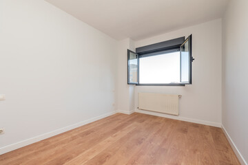 Empty room with open window, aluminum radiator and oak floor.
