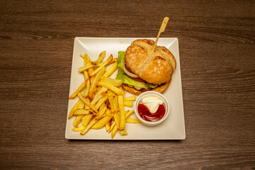 Top view of hamburger garnished with french fries, sauces, white onion and tomato