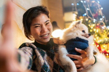 young asian female adult hand using smartphone taking selfie photo with her little puppy dog with smiling and happiness feeling in christmas and new year festive weekend holiday vacation at home