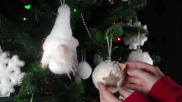 Woman hands hangs fluffy Christmas ball in decorated tree, closeup