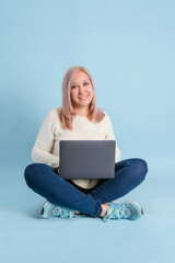 An adult female freelancer with a laptop on her lap sits on a blue background